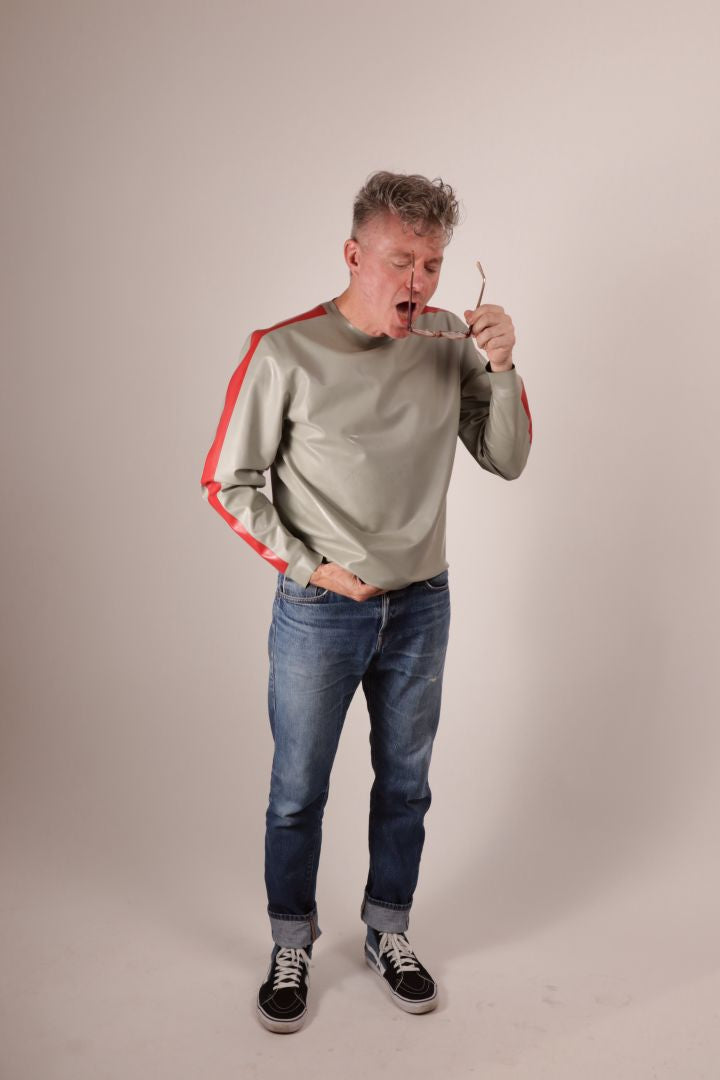 Fabian trying to clean his glasses in his grey latex sweatshirt with red stripes on the arms.