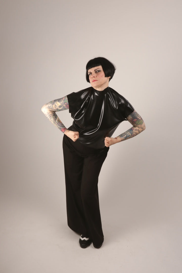 Anja in our black sleeveless latex 60s top and black sailor pants flexing her arm muscles towards the camera.