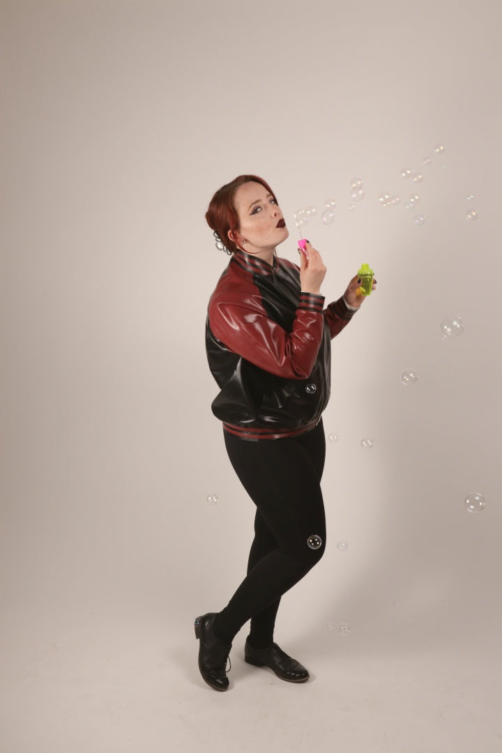 Sarah wearing her black and maroon zippered college jacket and blowing soap bubbles.