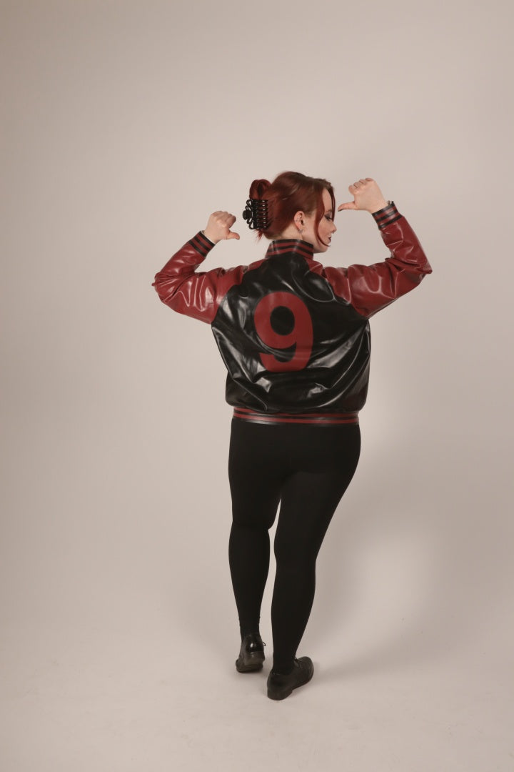 Total of Sarah proudly pointing at the number on the back of her TARZA & JANE latex varsity jacket.