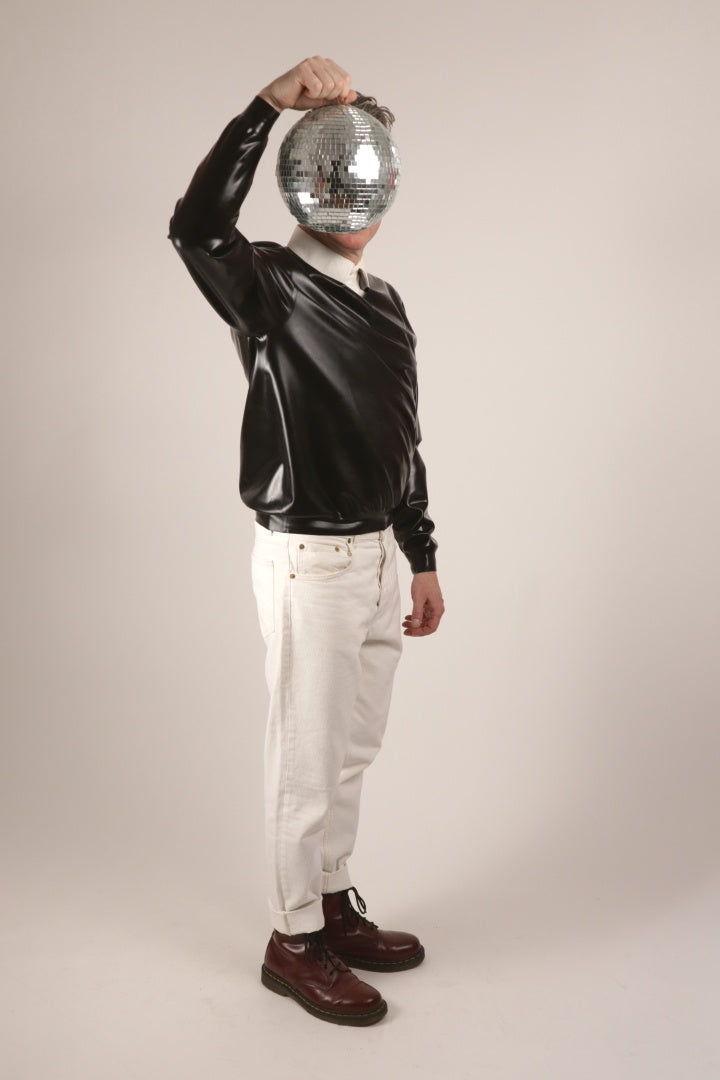 Fabian wearing his black V-neck latex sweater over a white dress shirt. And he's holding up a disco mirror ball and hiding his face.