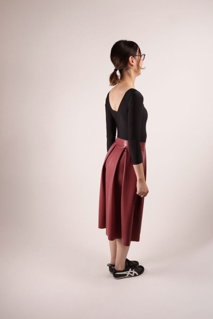 Side rear view of our model Hani in our TARZA & JANE bordeaux red midi latex skirt with box pleats