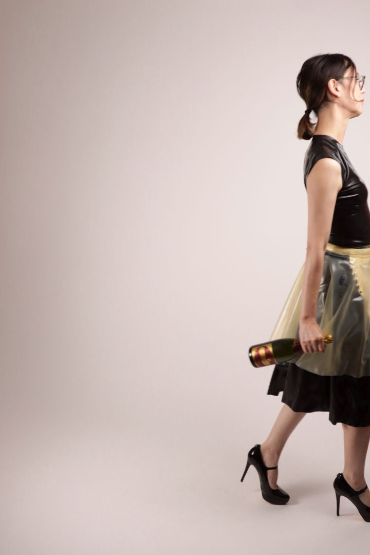 Our model Hani determinedly leaving the set with a bottle of champagne dangling from her right hand. All of this in our TARZA & JANE impossible latex maid dress. A conservative black sleeveless latex dress with a white latex maids apron under a transparent flared mini skirt.