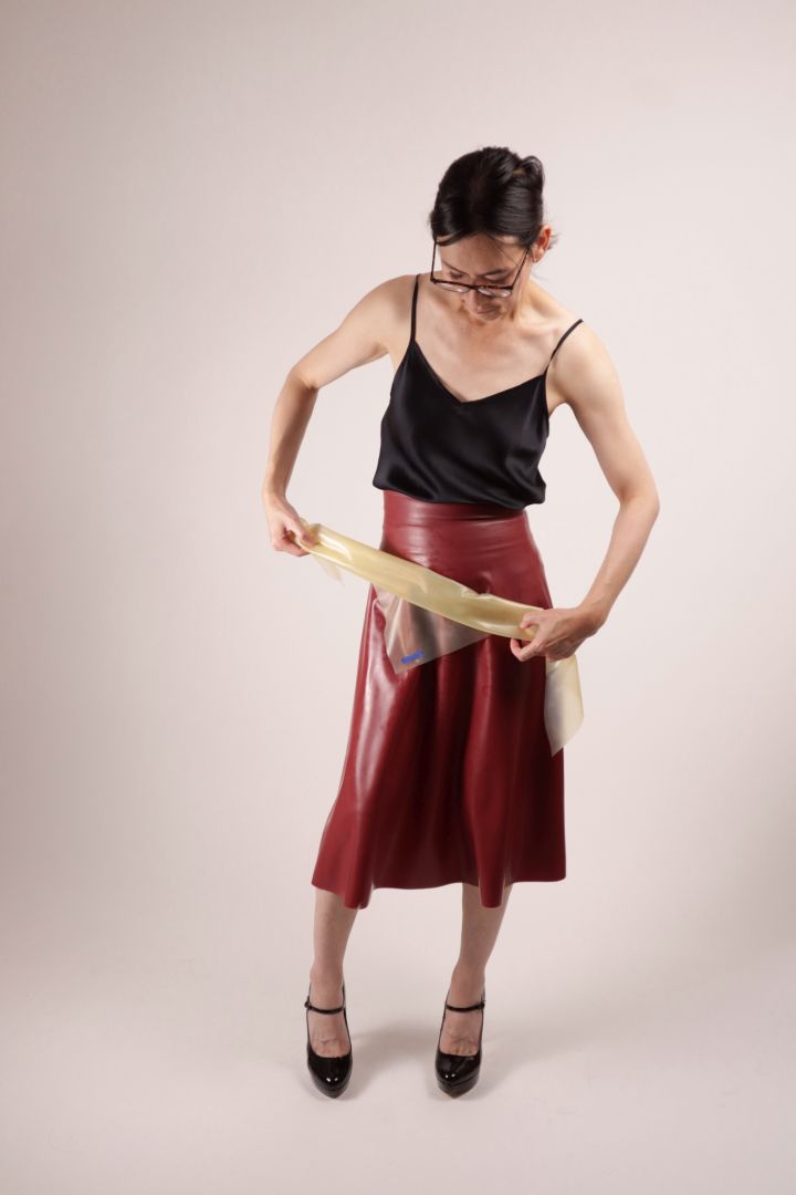 Hani rolling the TARZA & JANE transparent latex scarf triangle into a neck scarf. She also wears a dark red latex midi skirt.