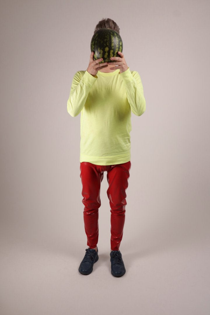 Fabian in loose red TARZA & JANE latex leggings, a neon yellow longsleeve and blue camper sneakers holding a watermelon in front of his face. An hommage to 'I carried a watermelon' scene in the movie 'dirty dancing' with Patrick Swayze.