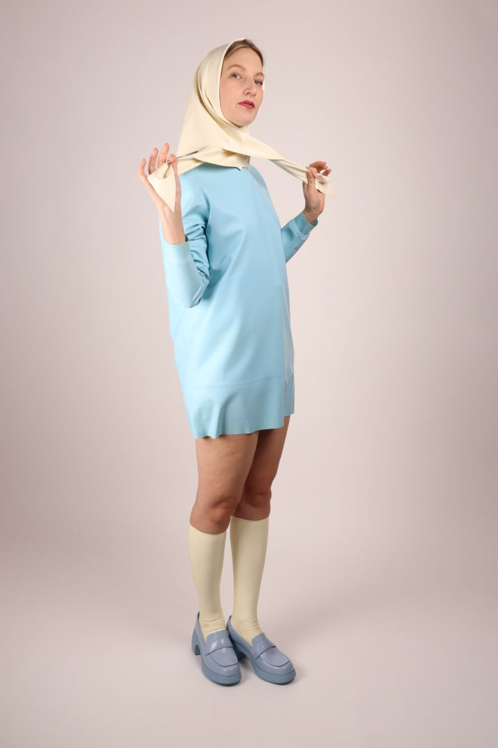 model in baby blue sweatshirt dress and matching camper shoes is adjusting a white latex headscarf