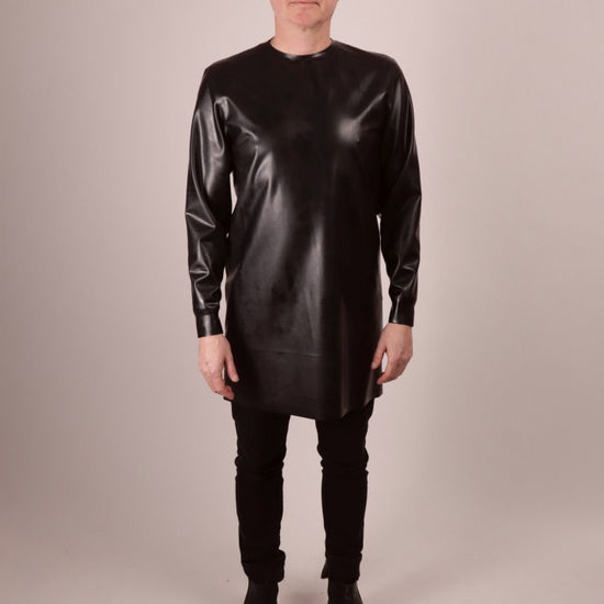 a video of Fabian walking into focus wearing a black latex long sweatshirt over black skinny jeans and pointy black shoes.