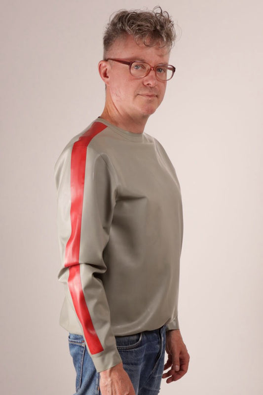 Close-up of Fabian in blue jeans and his grey latex loose sweater with red arm stripes.