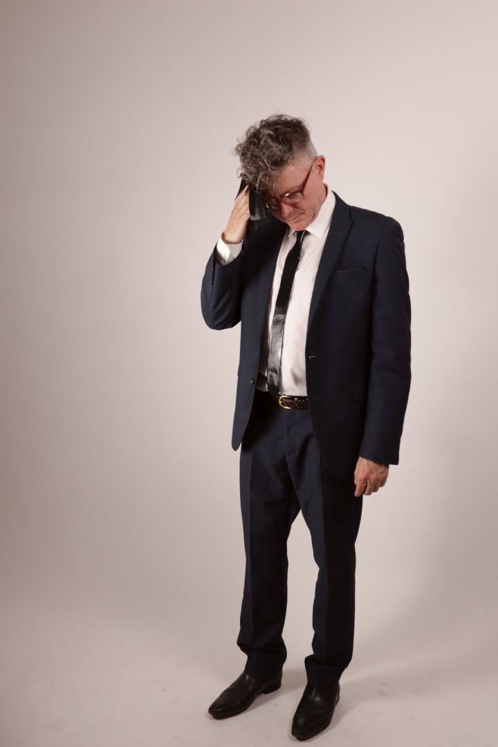 Our model Fabian wiping his brow with a black pocket square. He's wearing a navy blue business suit with a white dress shirt and his favorite new black latex tie. 