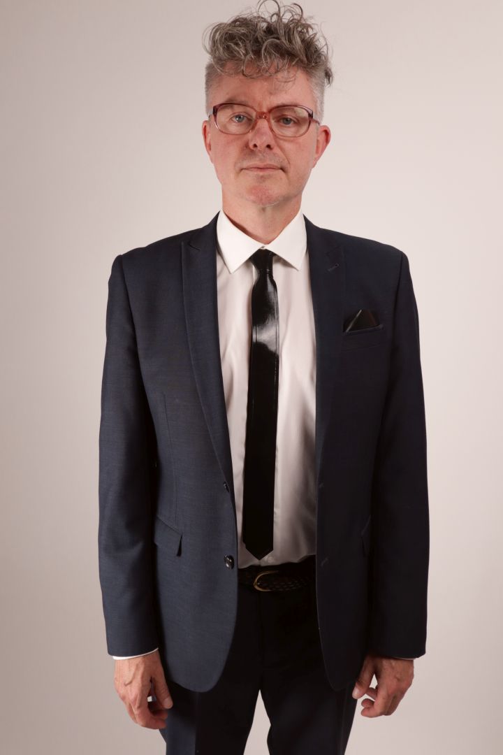 Frontal view of our model Fabian in his navy blue business suit and white dress shirt and black narrow latex tie with matching latex pocket square.