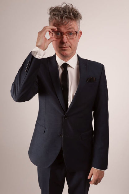 Fabian repositioning his glasses. He's in his navy blue business suit, white dress shirt and black narrow latex tie.