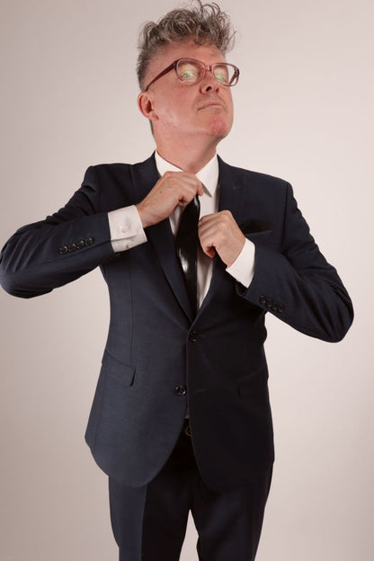 Fabian in his navy blue business suit and white dress shirt tightening his black narrow latex tie.
