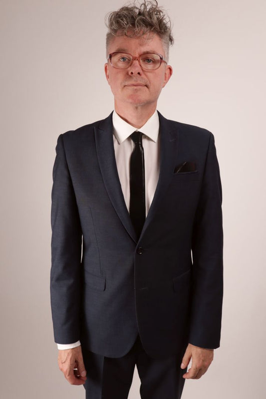 Frontal view of our model Fabian in his navy blue business suit and white dress shirt and his black narrow latex neck tie with matching latex pocket square.
