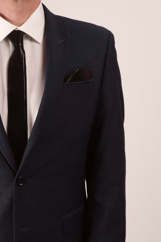 Our designer Fabian in a close-up wearing a navy blue business suit with a white dress shirt and his favorite new black latex tie. and he has a matching black latex pocket square tucked into the jacket's breast pocket.