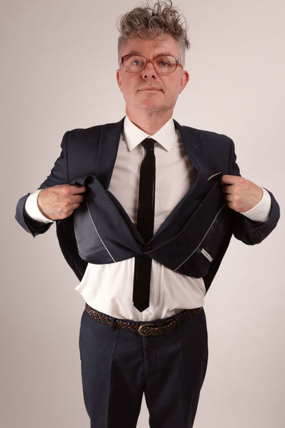 Fabian in his navy blue business suit and white dress shirt lifting his jacket up to show off his black narrow latex tie.
