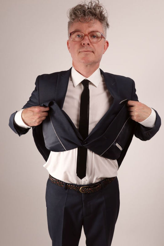 Fabian in his navy blue business suit and white dress shirt lifting his jacket up to show off his black narrow latex tie.