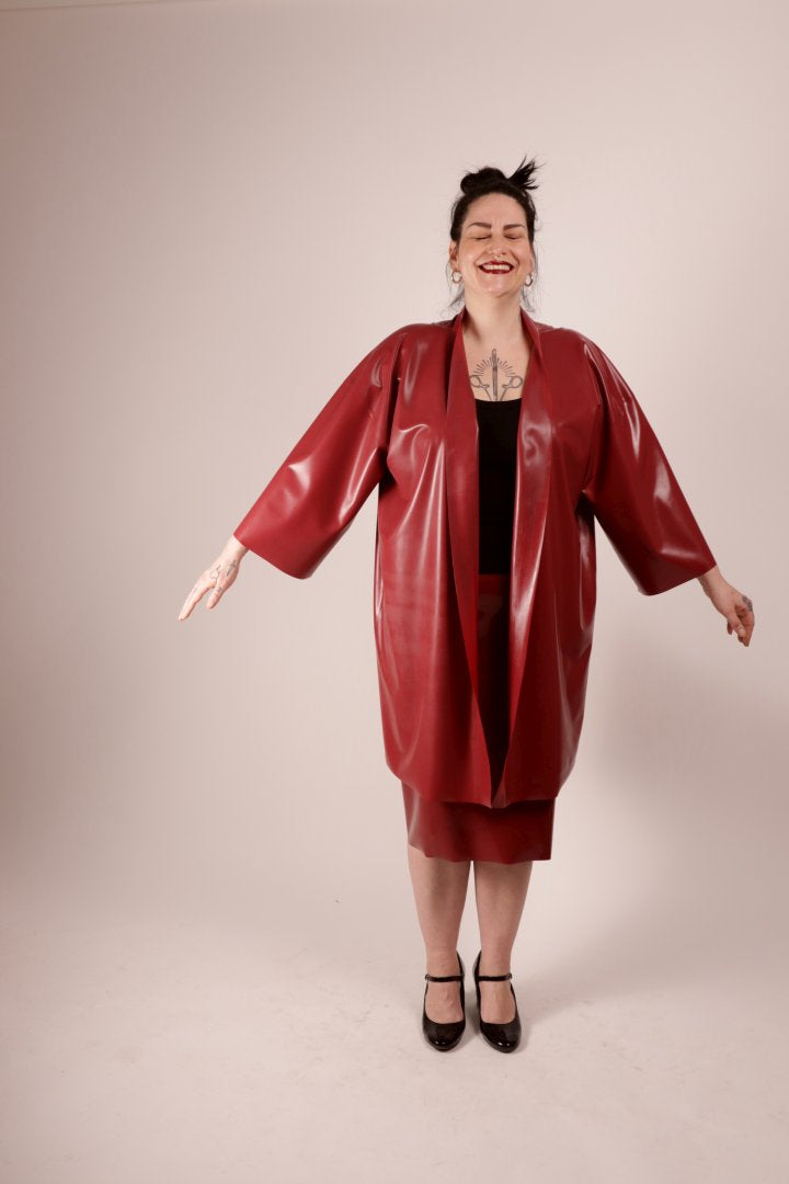 our model sadic sadie in our wine red latex fashion kimono and matching pencil skirt, with her arms lifted a quarter and laughing with her eyes closed