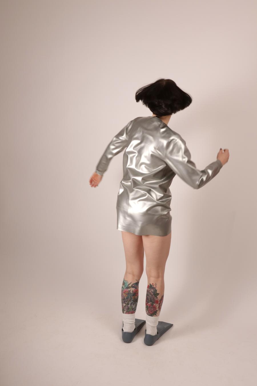 back view of Anja Abels dancing in silver latex sweatshirt dress and tennis socks and fins