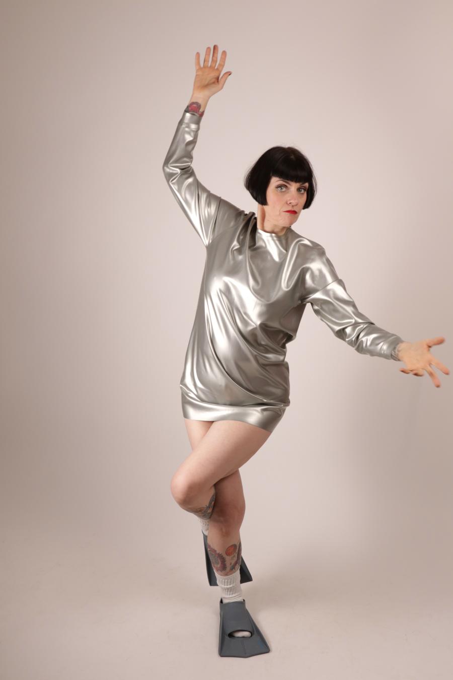 Anja Abels in a silver latex sweatshirt dress standing on one leg