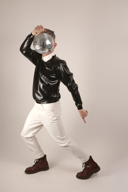 Fabian disco dancing in his black V-neck latex sweater over a white dress shirt. And he's holding up a disco mirror ball and hiding his face.