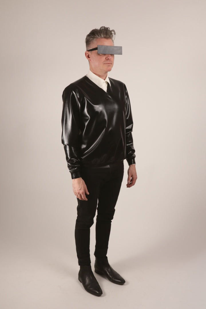 Fabian wearing a black V-neck latex sweater over a white dress shirt and with skinny black pants and pointy chelsea boots.