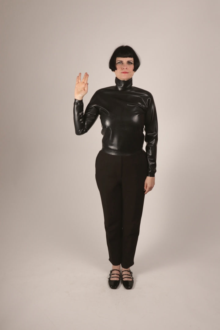 Our model Anja doing a vulcanian v greet in a black latex turtleneck sweater top and her mary janes. Front view.