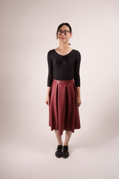 Model Hani standing alert in a dark red demi latex pleat skirt by TARZA & JANE