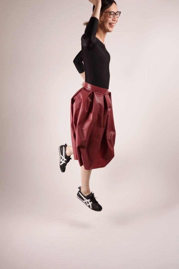 Model Hani jumping in a bordeaux red midi latex skirt with box pleats