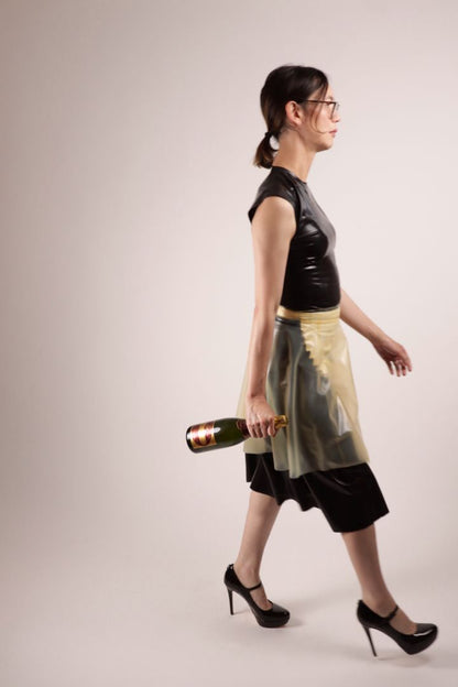 Our model Hani resolutely walking off the set with a bottle of champagne dangling from her right hand. All of this in our TARZA & JANE impossible latex maid dress. A conservative black kneelength dress with a white latex maids apron under a transparent flared mini skirt. She seems to have better plans.