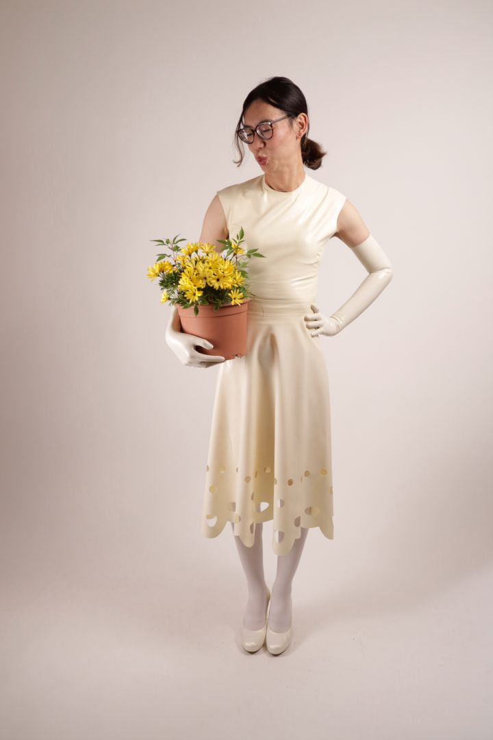 Hani posing in our TARZA & JANE lacey wedding dress. The sleeveless top with wide shoulders and a t-shirt neckline looks just lovely with the midi skirt and its lace pattern hem. Hani throws a kiss to the pot with yellow flowers.