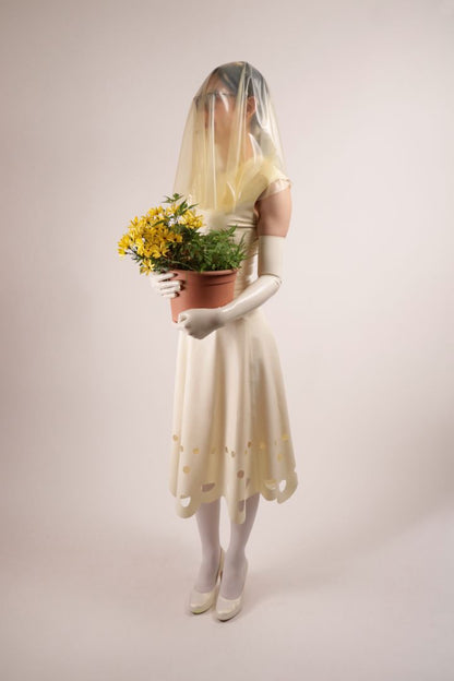 Side view of Hani modelling our TARZA & JANE lacey wedding dress. Her face is hidden by her transparent latex veil. She is holding the flower pot bouquet. Very Sustainable. Catch!