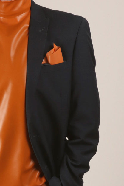 Our designer Fabian in a close-up wearing a navy blue business suit with his favorite orange latex turtleneck. and he has a matching orange latex pocket square tucked into the jackets breast pocket.