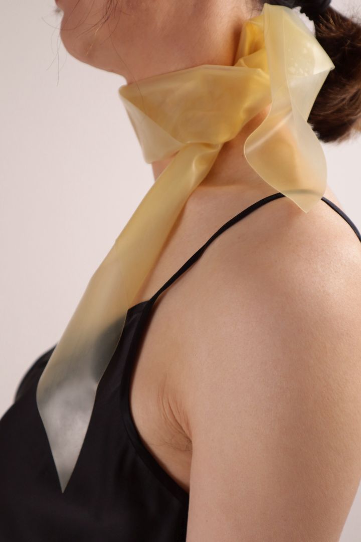 Close-up of Hani wearing the  transparent latex scarf around her neck. Knot detail seen from the left.